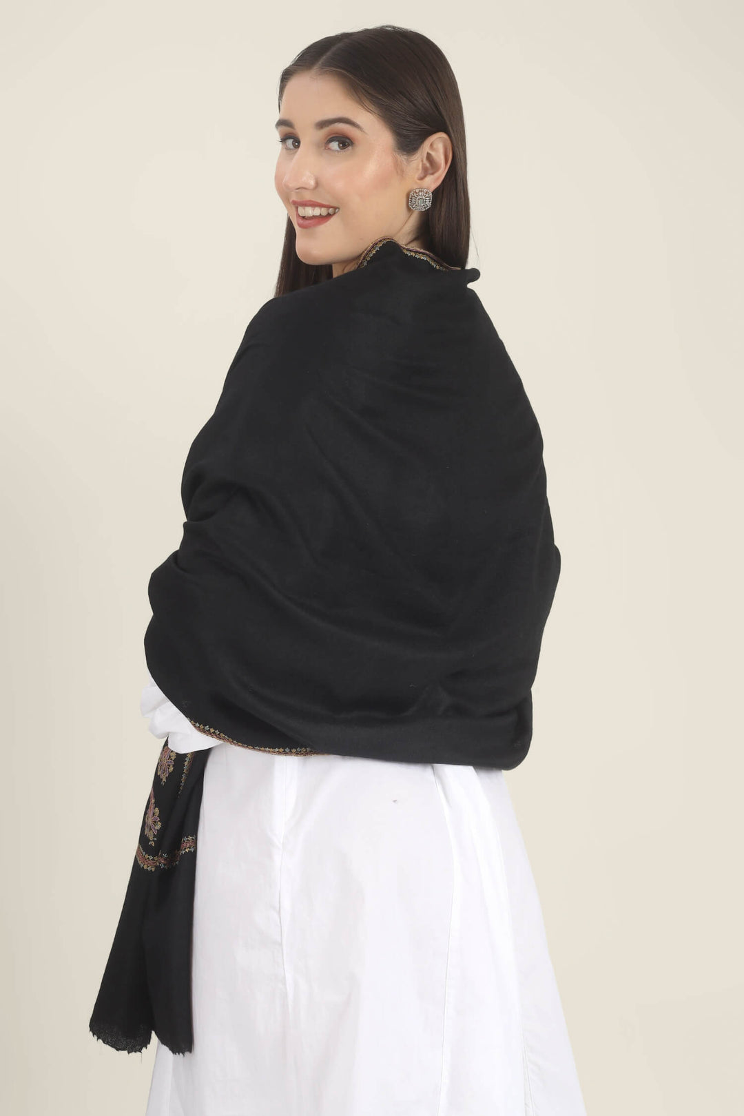Model wearing a black GI Kashmiri Pure Pashmina stole with multicolour paisley Sozni embroidery on the borders over a white outfit.