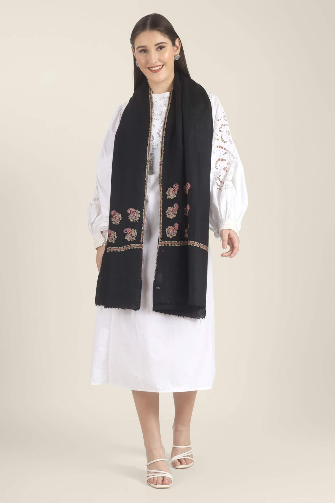 Model wearing a black GI Kashmiri Pure Pashmina stole with multicolour paisley Sozni embroidery on the borders over a white outfit.