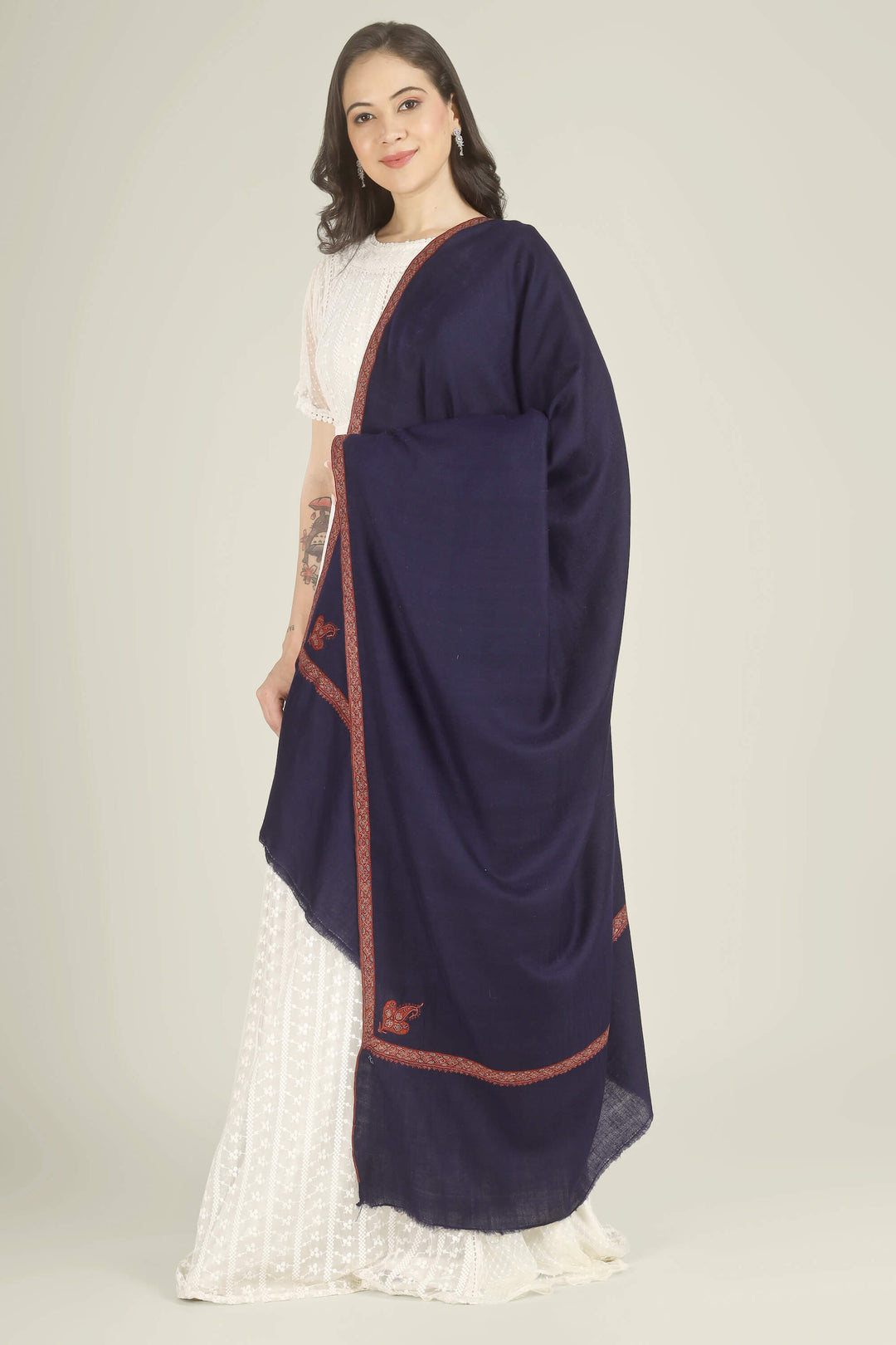A woman modeling a dark navy blue shawl with rust-red embroidered borders, draped over a white traditional outfit against a plain light beige background.