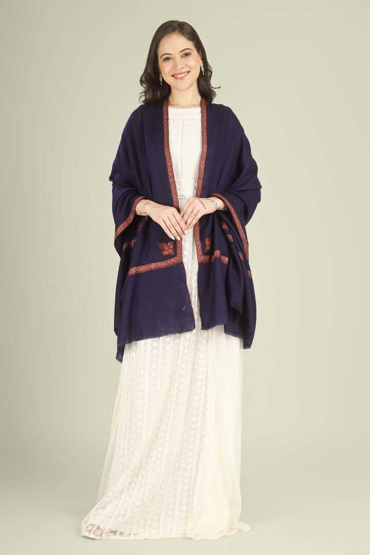 A woman modeling a navy blue shawl with red embroidered borders over a white dress, photographed against a solid light beige studio background.
    
      | pashmina shawls online | authentic Kashmiri pashmina shawl online | pure pashmina shawl online | original GI certified pashmina shawl online | luxury men's pashmina shawl online from Kashmir | where to buy online pure pashmina in India
    
    | GI Tag Certified - Government-verified authentic Kashmiri Pashmina
    | G20 Official Partner - Selected by India for G20 Summit gifting
    | Handicraft Registered - Official recognition of traditional craftsmanship
    | Certificate of Authenticity - Every purchase includes GI certification