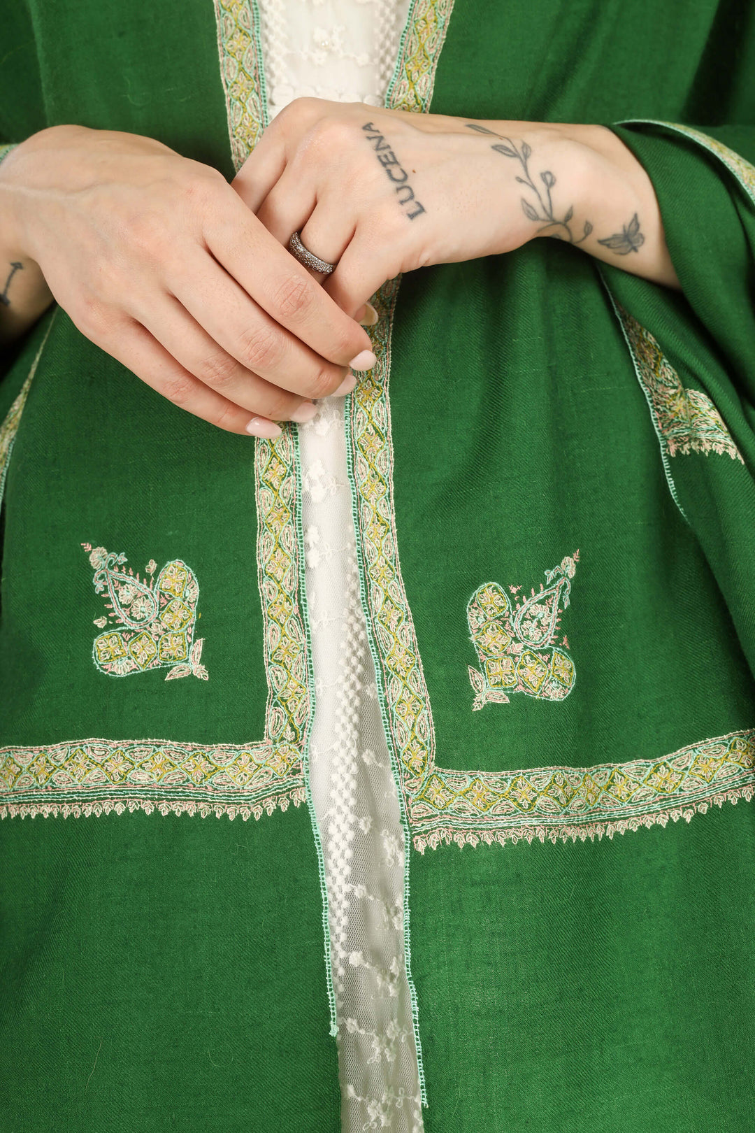 Close-up of a person wearing a green embroidered garment with white lace trim and decorative motifs on the chest, with both hands visible adjusting the front.