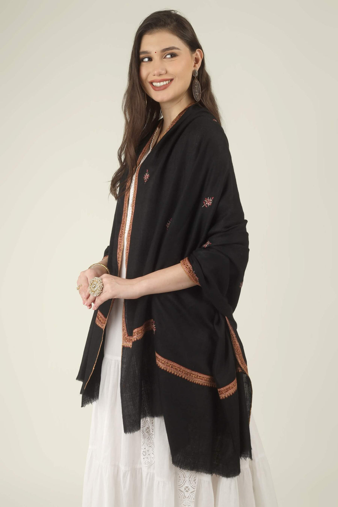 This Black GI Kashmiri Pure Pashmina Hashidaar Embroidered Shawl features a deep, solid black body framed by a richly worked border in copper, rust and soft pink, with small floral buti motifs scattered across the ground.