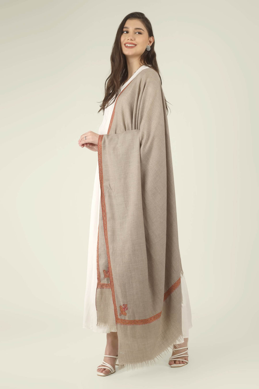This Natural Khudrang GI Kashmiri Pure Pashmina Border Embroidered Shawl features a beautifully textured, undyed oatmeal-beige body. It is elegantly framed by continuous, richly worked red and orange borders