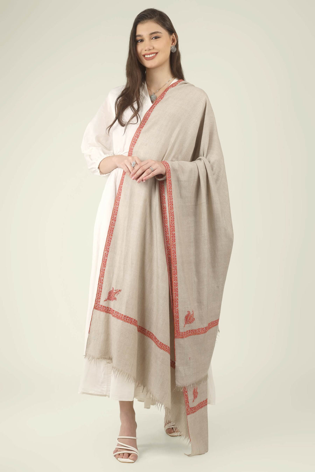 This Natural Khudrang GI Kashmiri Pure Pashmina Hashidaar Embroidered Shawl features a soft, undyed oatmeal-beige body framed by richly worked borders and paisley motifs in vivid red and warm orange