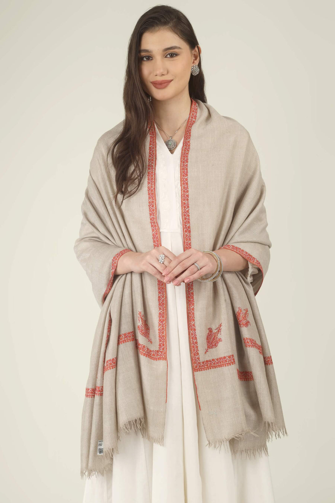 This Natural Khudrang GI Kashmiri Pure Pashmina Hashidaar Embroidered Shawl features a soft, undyed oatmeal-beige body framed by richly worked borders and paisley motifs in vivid red and warm orange