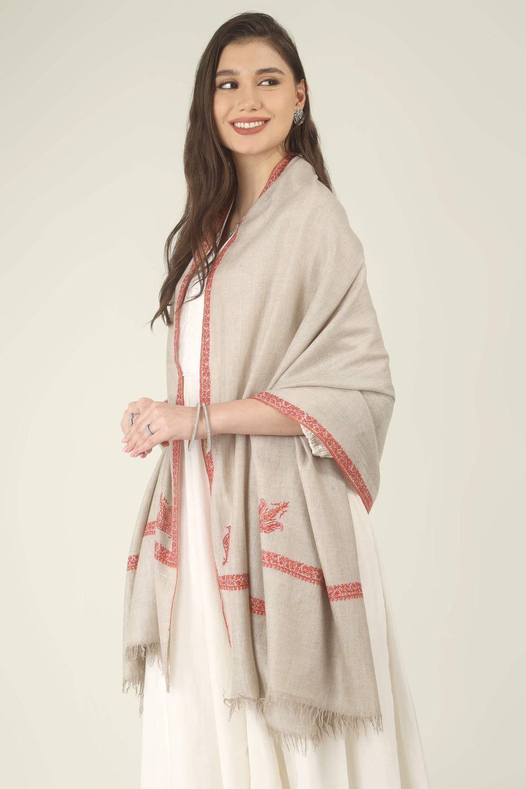 This Natural Khudrang GI Kashmiri Pure Pashmina Hashidaar Embroidered Shawl features a soft, undyed oatmeal-beige body framed by richly worked borders and paisley motifs in vivid red and warm orange