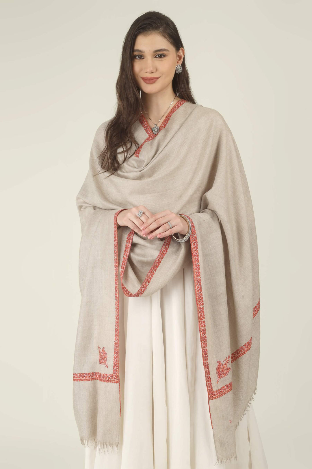 This Natural Khudrang GI Kashmiri Pure Pashmina Hashidaar Embroidered Shawl features a soft, undyed oatmeal-beige body framed by richly worked borders and paisley motifs in vivid red and warm orange