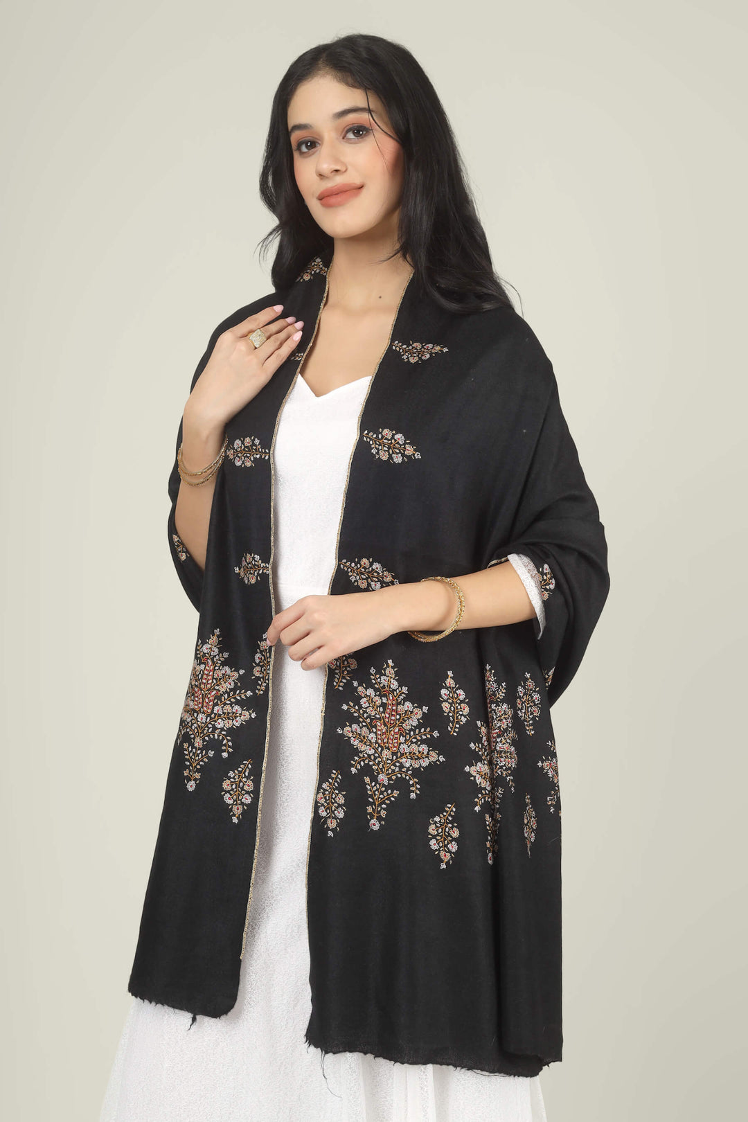 Model wearing a black GI Kashmiri Pure Pashmina stole with delicate multicolour floral Sozni embroidery over a white dress.