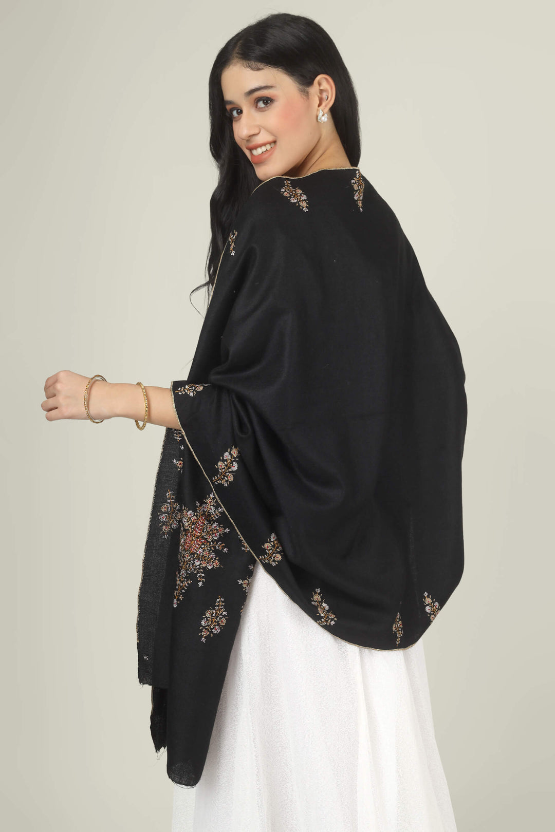 Model wearing a black GI Kashmiri Pure Pashmina stole with delicate multicolour floral Sozni embroidery over a white dress.