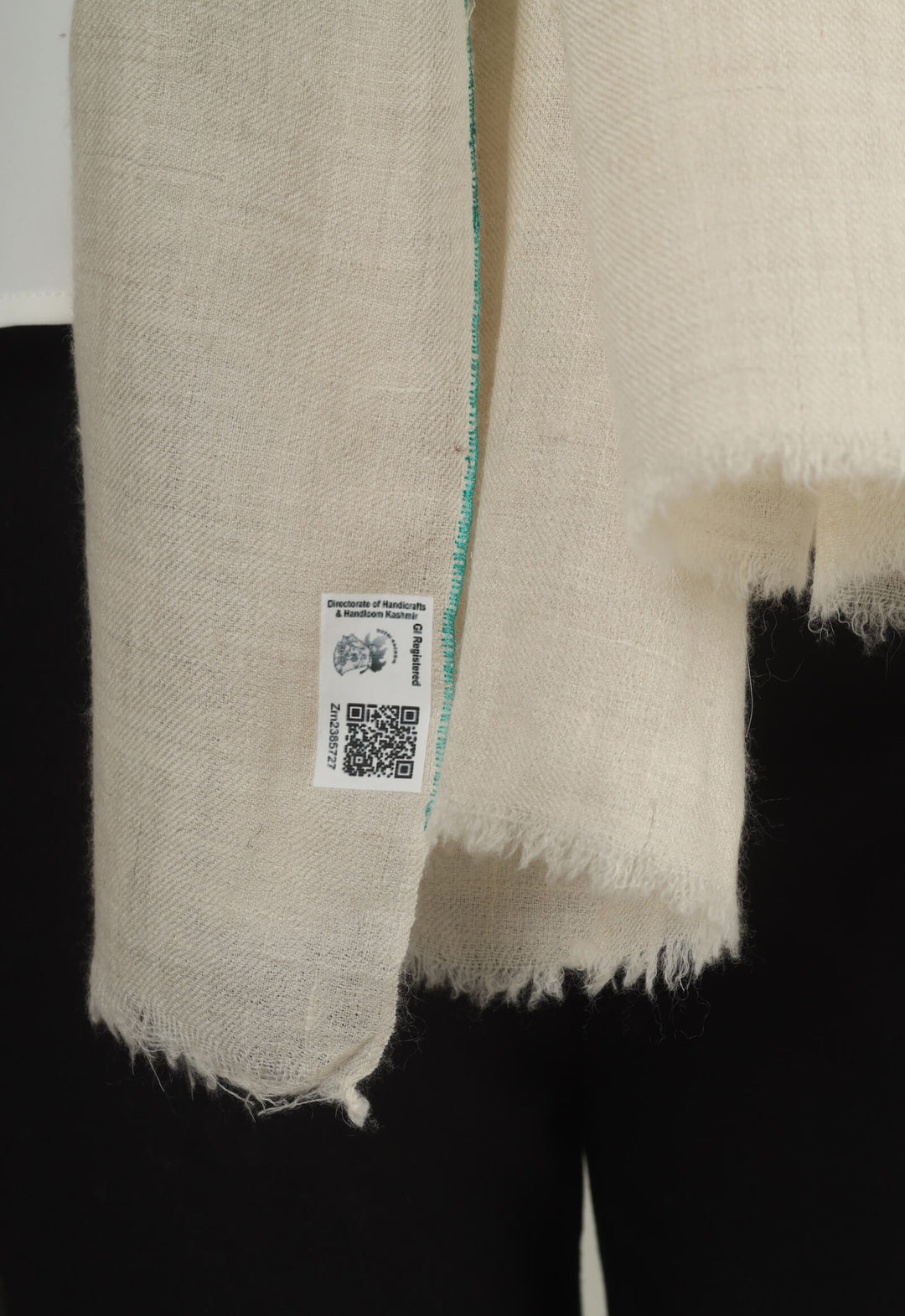 Close-up of a white GI Kashmiri Pure Pashmina stole with turquoise-green floral jaal Sozni embroidery knotted at the front over a white shirt.