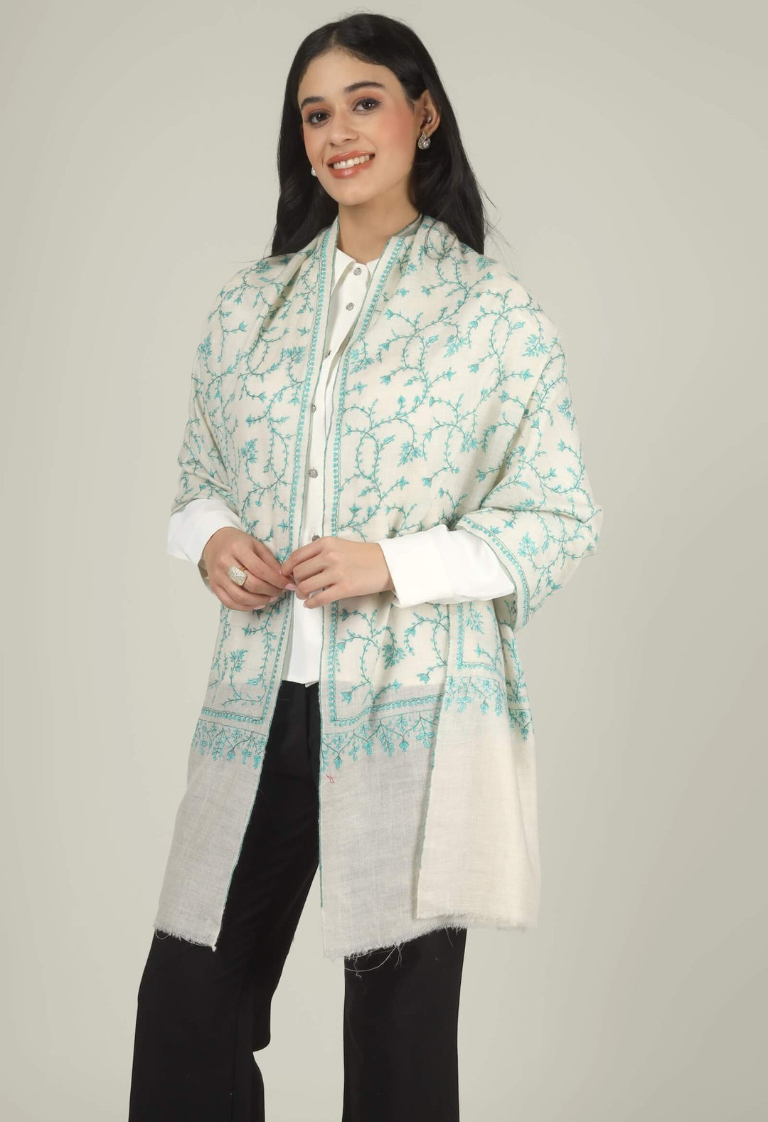 Close-up of a white GI Kashmiri Pure Pashmina stole with turquoise-green floral jaal Sozni embroidery knotted at the front over a white shirt.