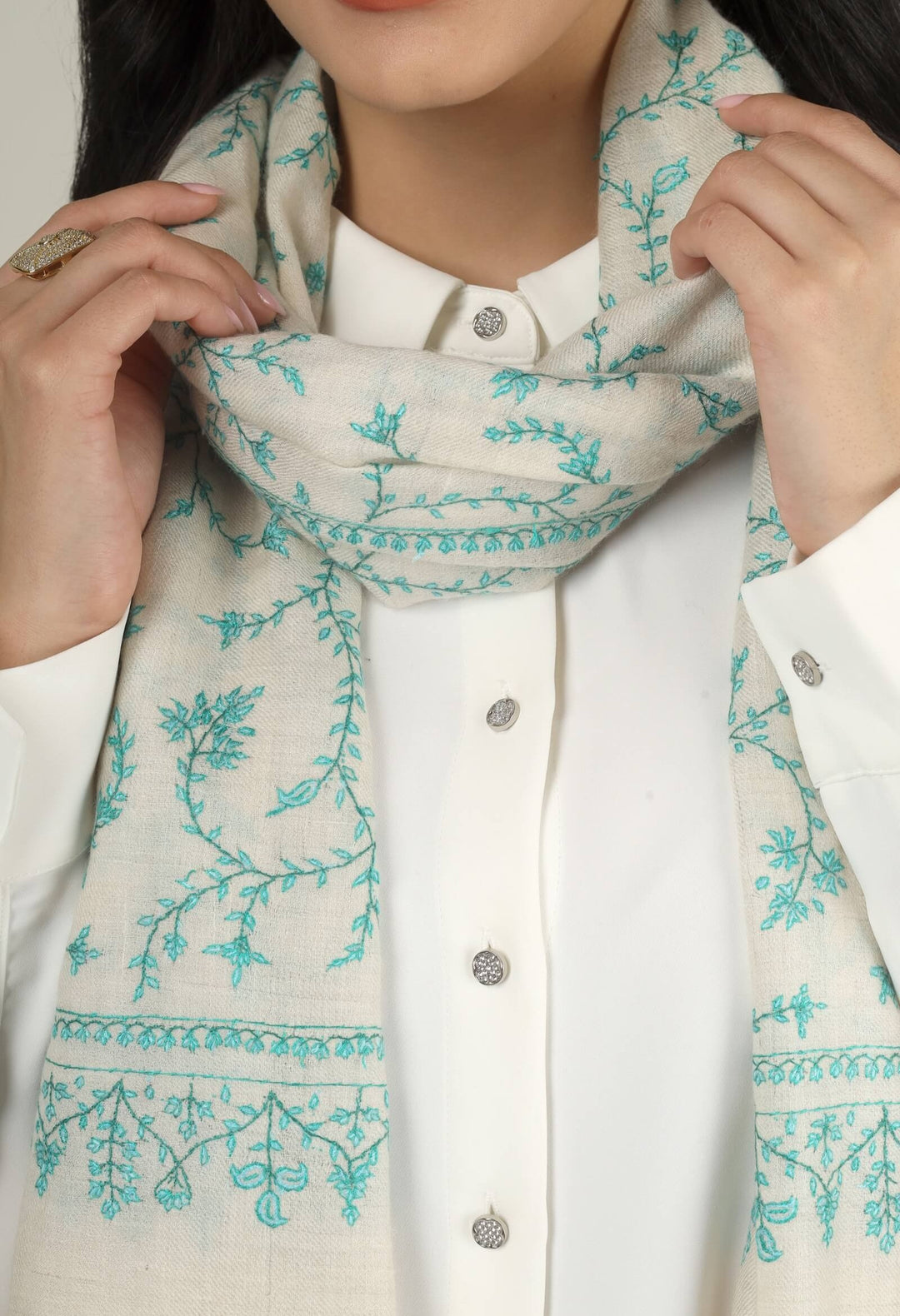 Close-up of a white GI Kashmiri Pure Pashmina stole with turquoise-green floral jaal Sozni embroidery knotted at the front over a white shirt.