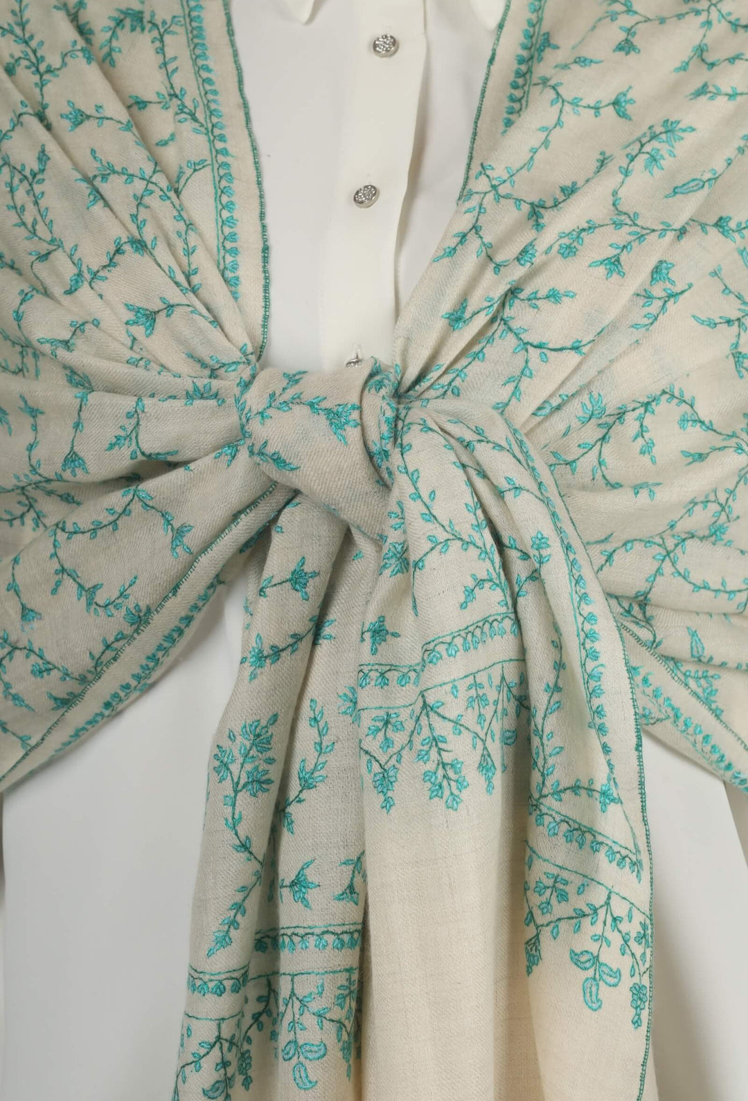 Close-up of a white GI Kashmiri Pure Pashmina stole with turquoise-green floral jaal Sozni embroidery knotted at the front over a white shirt.