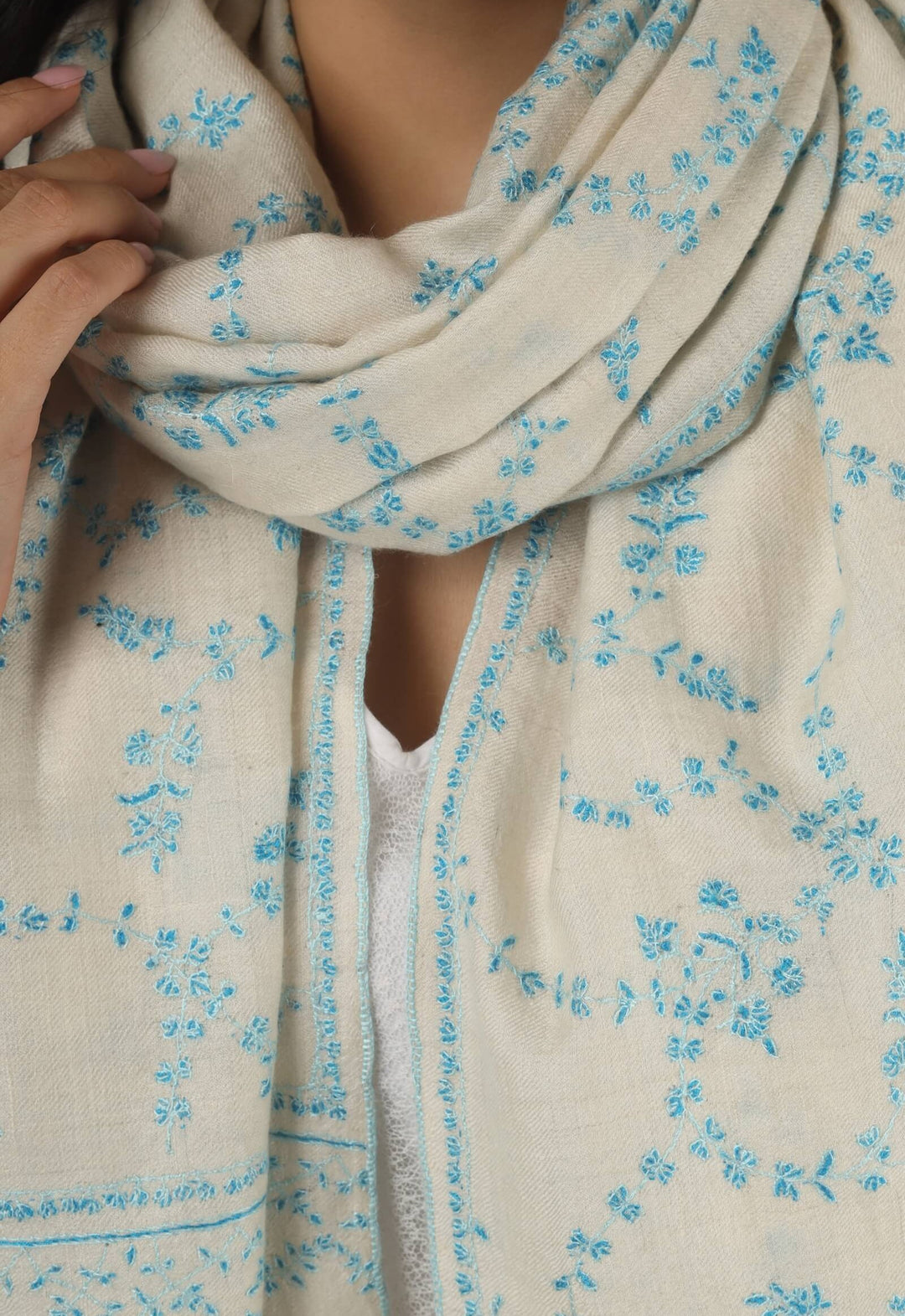Close-up of a white GI Kashmiri Pure Pashmina stole with delicate sky-blue floral Sozni embroidery draped around the neck.