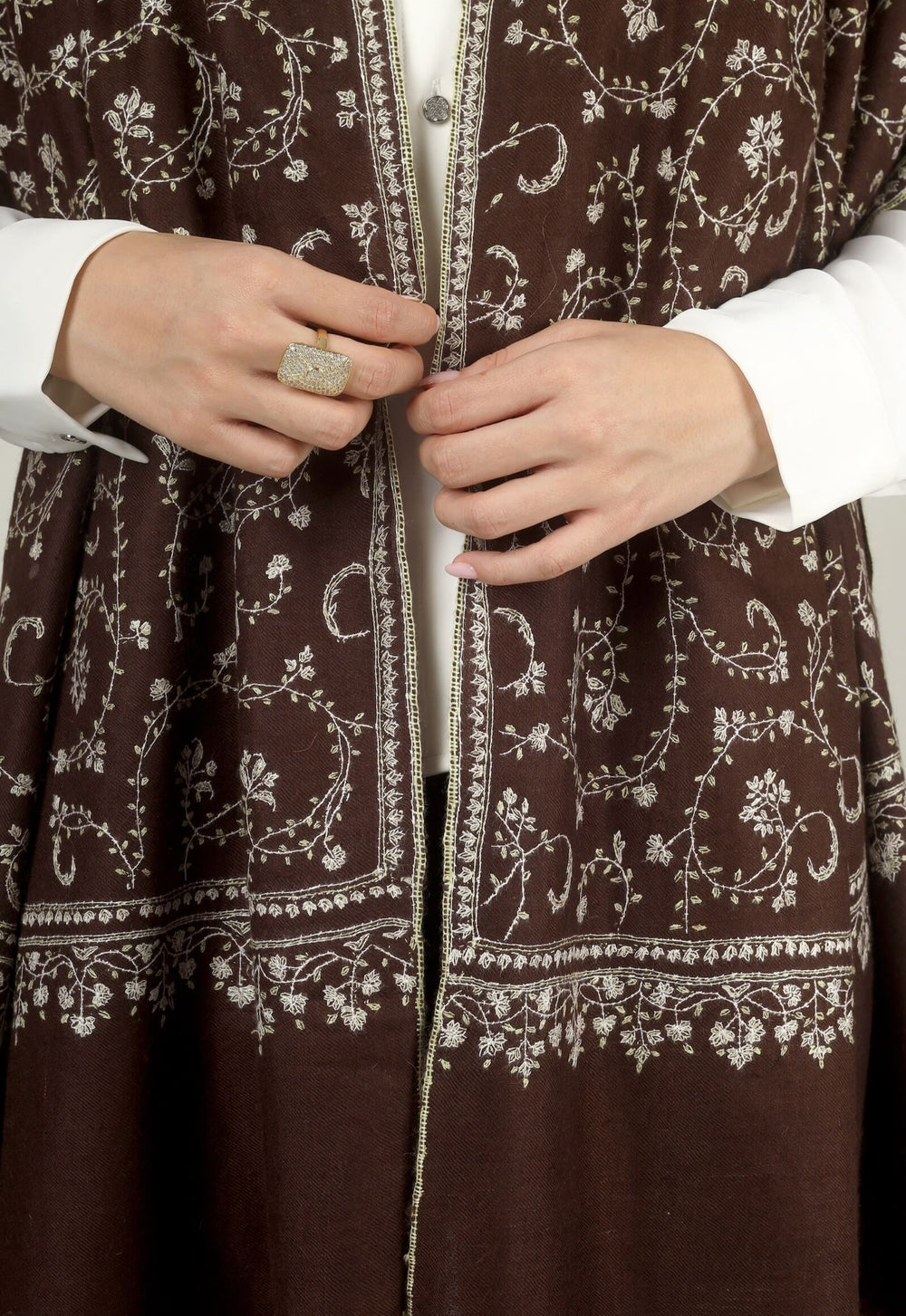 Close-up of a brown GI Kashmiri Pure Pashmina stole with ivory floral jaal and paisley Sozni embroidery worn open over a white shirt.