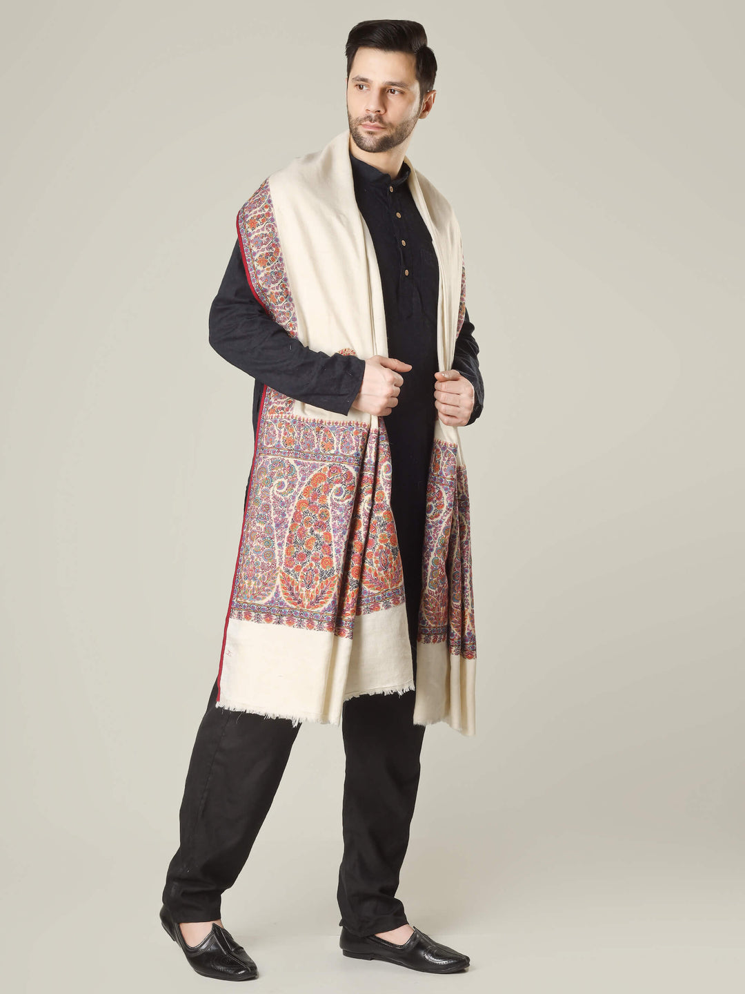 Antique Kashmiri kalamkari sozni men’s shawl with intricate multicolour paisley and floral embroidery on ivory pashmina, draped over a black kurta, handcrafted luxury wedding shawl from Kashmir.