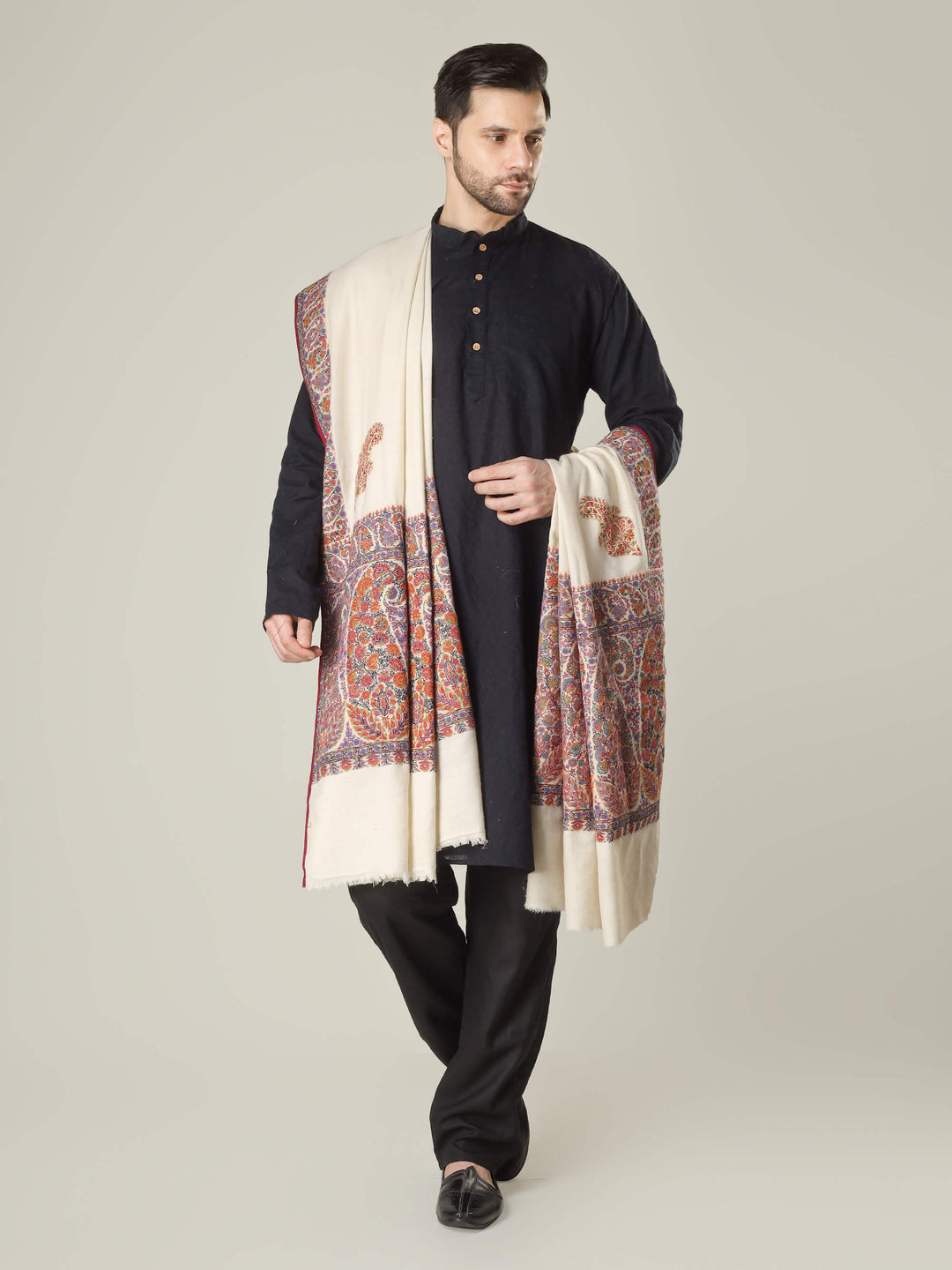 Antique Kashmiri kalamkari sozni men’s shawl with intricate multicolour paisley and floral embroidery on ivory pashmina, draped over a black kurta, handcrafted luxury wedding shawl from Kashmir.