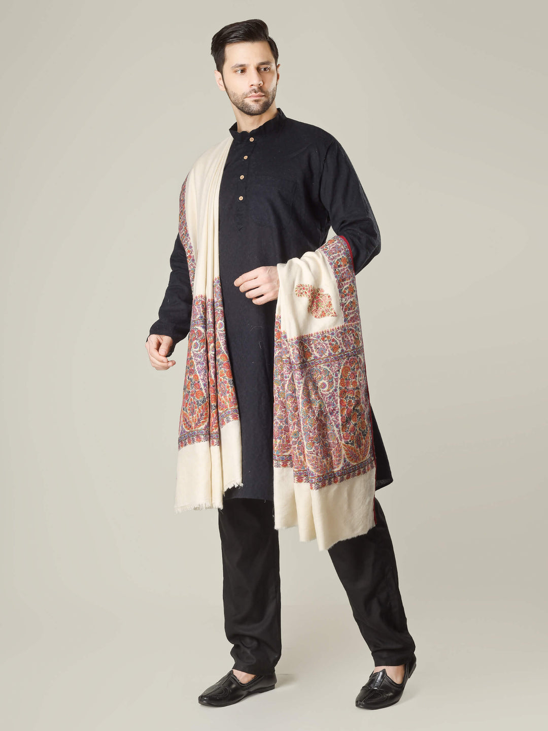 Antique Kashmiri kalamkari sozni men’s shawl with intricate multicolour paisley and floral embroidery on ivory pashmina, draped over a black kurta, handcrafted luxury wedding shawl from Kashmir.