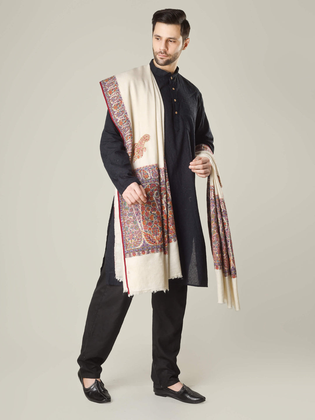 Antique Kashmiri kalamkari sozni men’s shawl with intricate multicolour paisley and floral embroidery on ivory pashmina, draped over a black kurta, handcrafted luxury wedding shawl from Kashmir.
