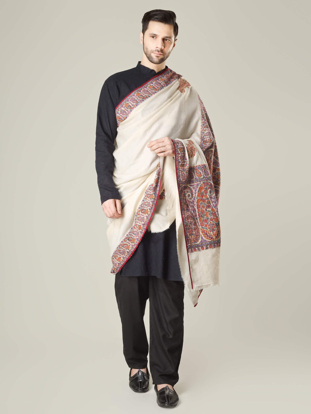 Antique Kashmiri kalamkari sozni men’s shawl with intricate multicolour paisley and floral embroidery on ivory pashmina, draped over a black kurta, handcrafted luxury wedding shawl from Kashmir.