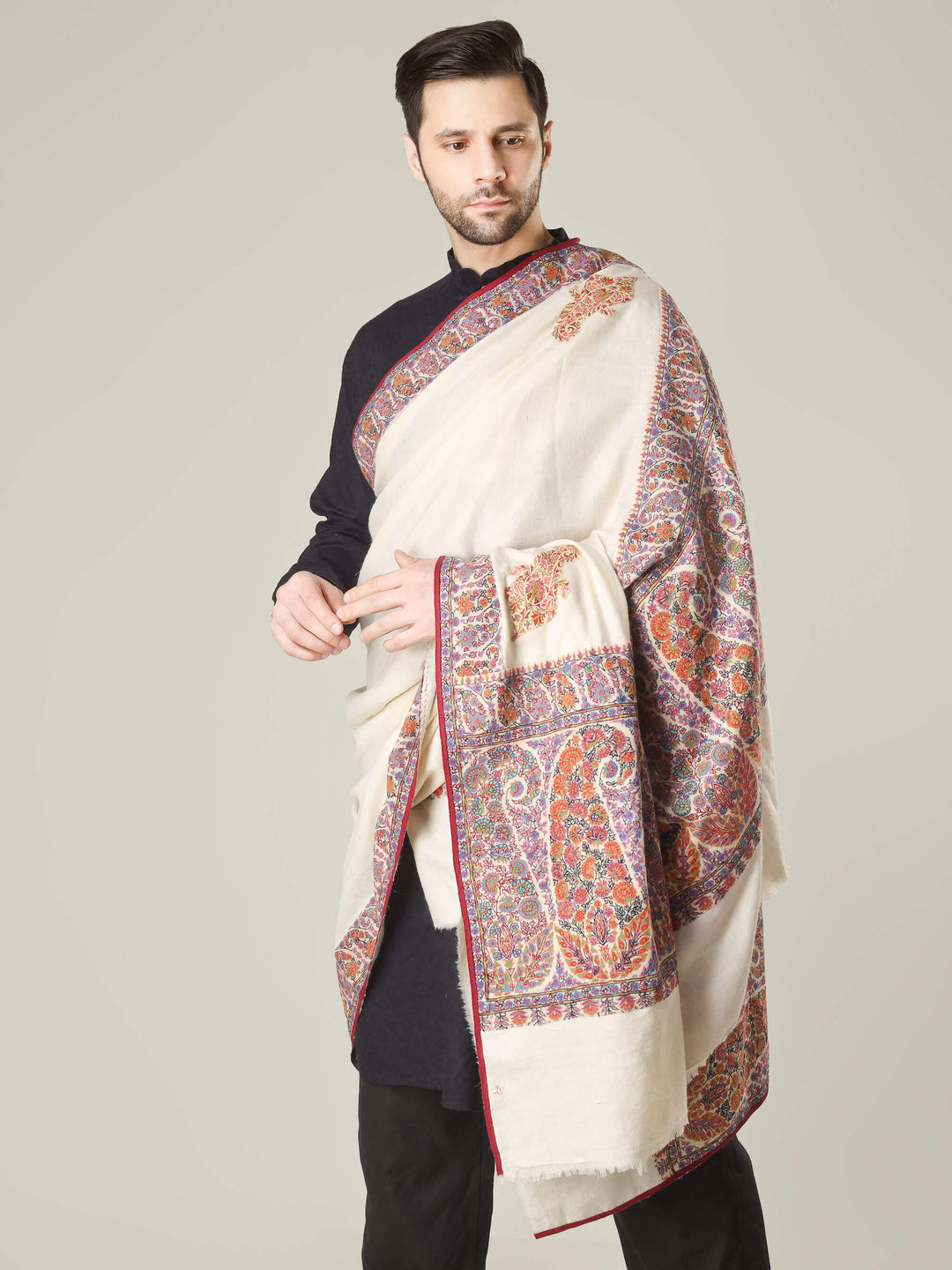 Antique Kashmiri kalamkari sozni men’s shawl with intricate multicolour paisley and floral embroidery on ivory pashmina, draped over a black kurta, handcrafted luxury wedding shawl from Kashmir.