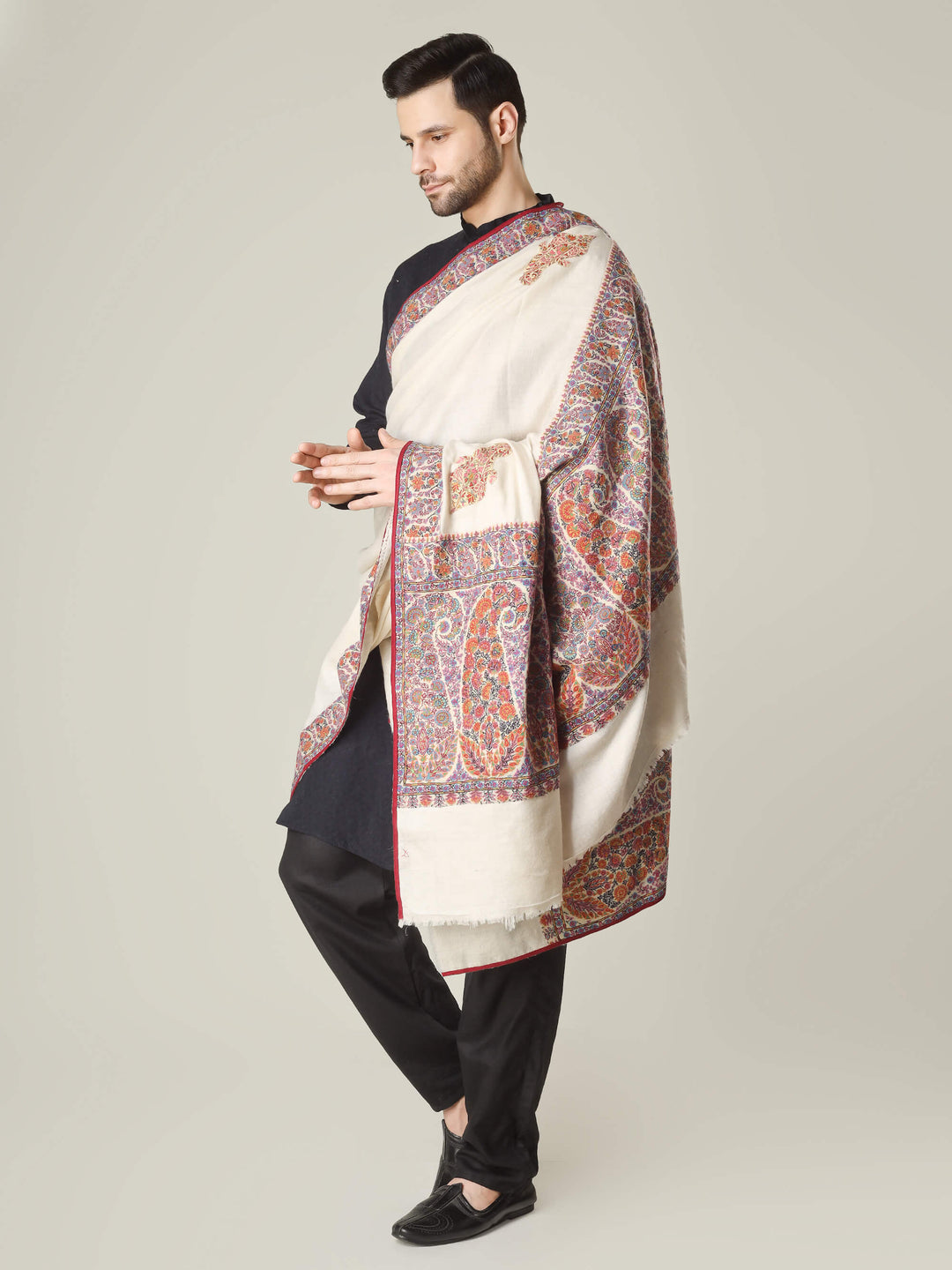 Antique Kashmiri kalamkari sozni men’s shawl with intricate multicolour paisley and floral embroidery on ivory pashmina, draped over a black kurta, handcrafted luxury wedding shawl from Kashmir.