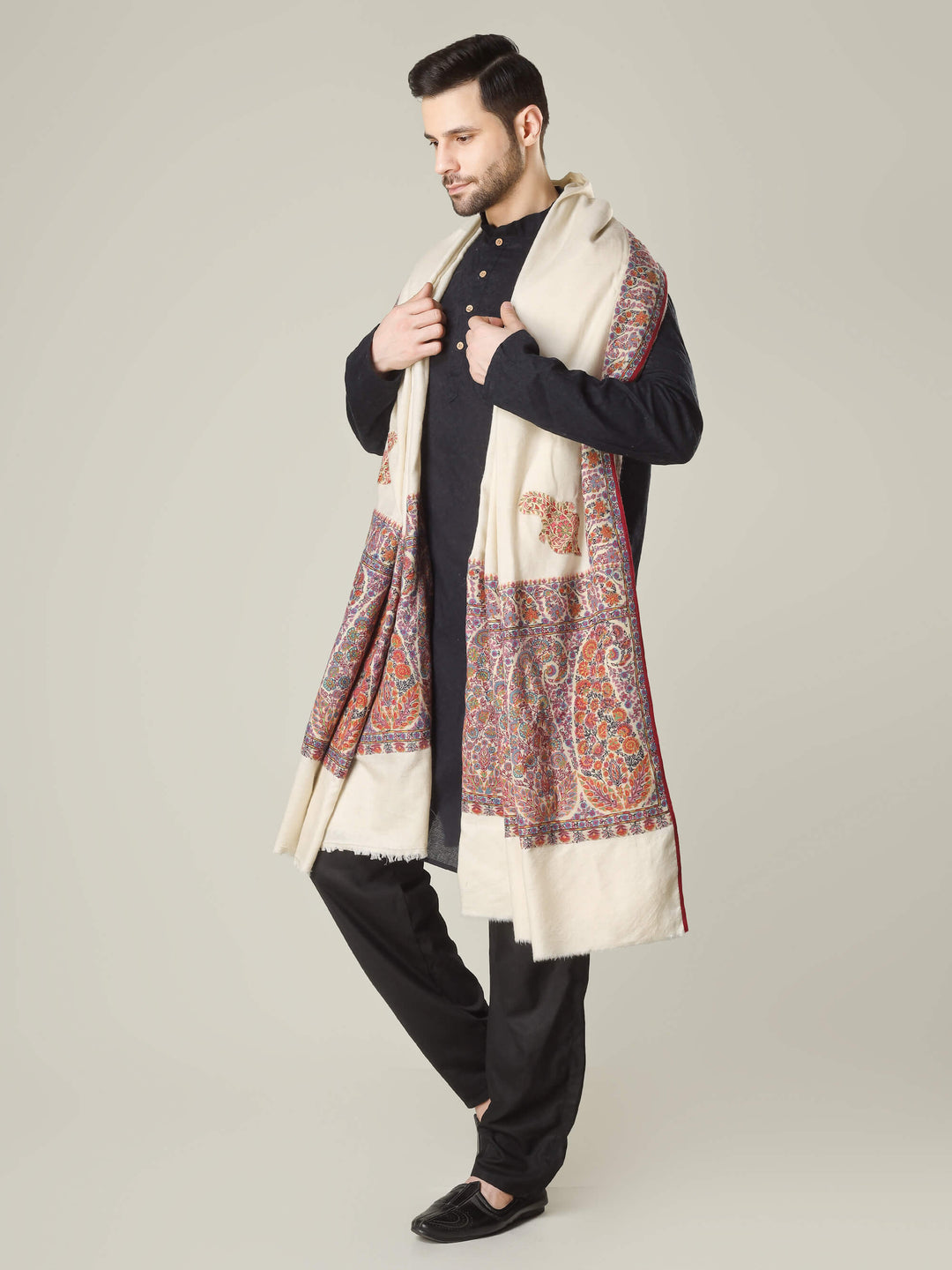 Antique Kashmiri kalamkari sozni men’s shawl with intricate multicolour paisley and floral embroidery on ivory pashmina, draped over a black kurta, handcrafted luxury wedding shawl from Kashmir.