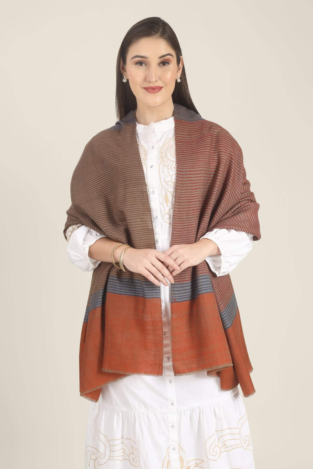 Model draped in a multicolour Pure Kashmiri Pashmina shawl with woven grey-blue, rust-red and taupe stripes and a wide plain rust border over a white embroidered dress.