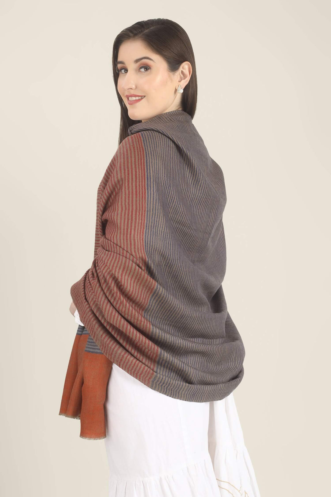 Model draped in a multicolour Pure Kashmiri Pashmina shawl with woven grey-blue, rust-red and taupe stripes and a wide plain rust border over a white embroidered dress.