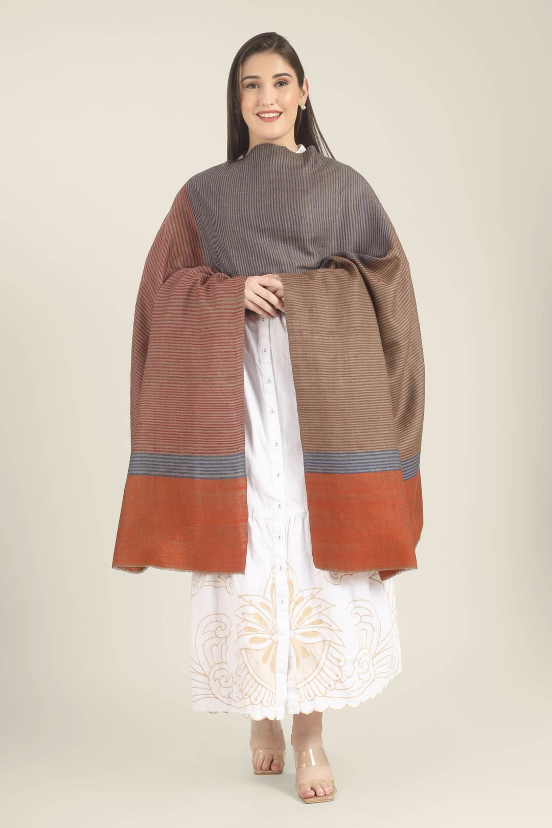 Model draped in a multicolour Pure Kashmiri Pashmina shawl with woven grey-blue, rust-red and taupe stripes and a wide plain rust border over a white embroidered dress.
