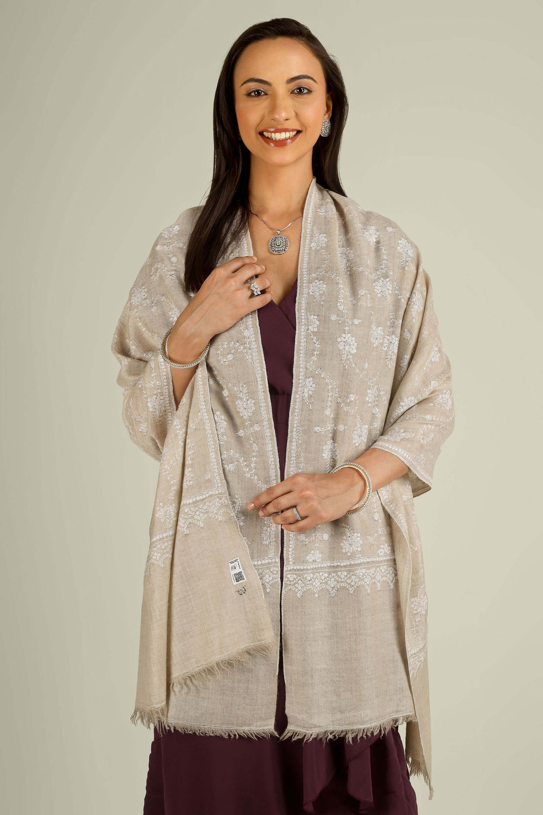 Beige GI Kashmiri pure pashmina embroidered stole by Kepra, draped on smiling model over plum dress, front view for Vienna winter styling