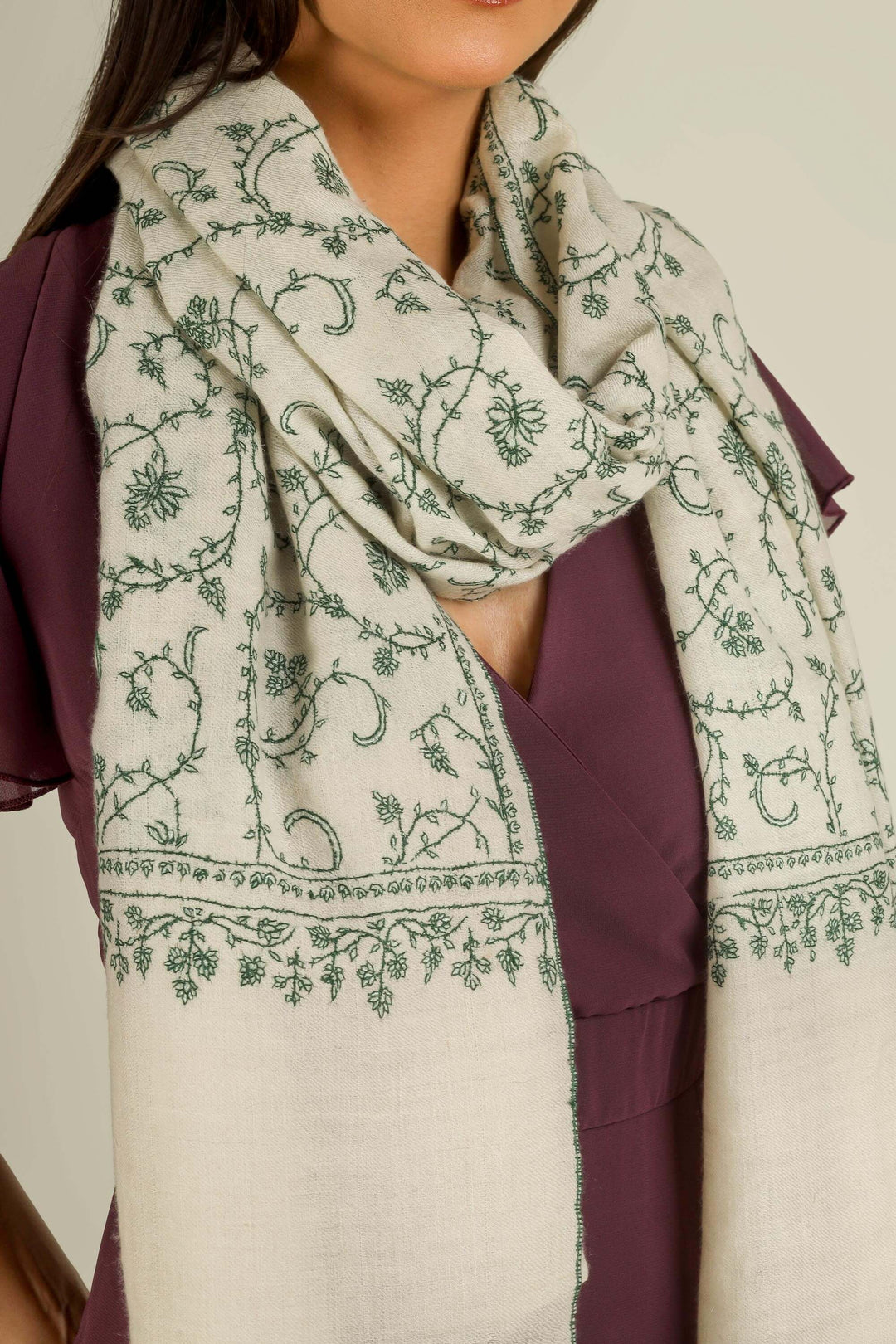 Ivory Kashmiri pure pashmina embroidered stole with green vine motifs by Kepra, wrapped around neck over plum dress, front detail view for Barcelona winter styling