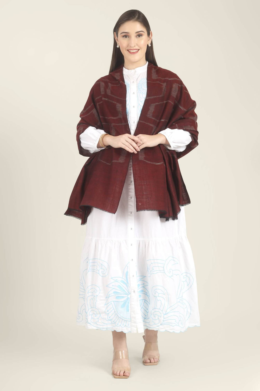 Model draped in a maroon Pure Kashmiri Pashmina shawl with a woven silvery grey geometric pattern over a white dress with light blue embroidery.