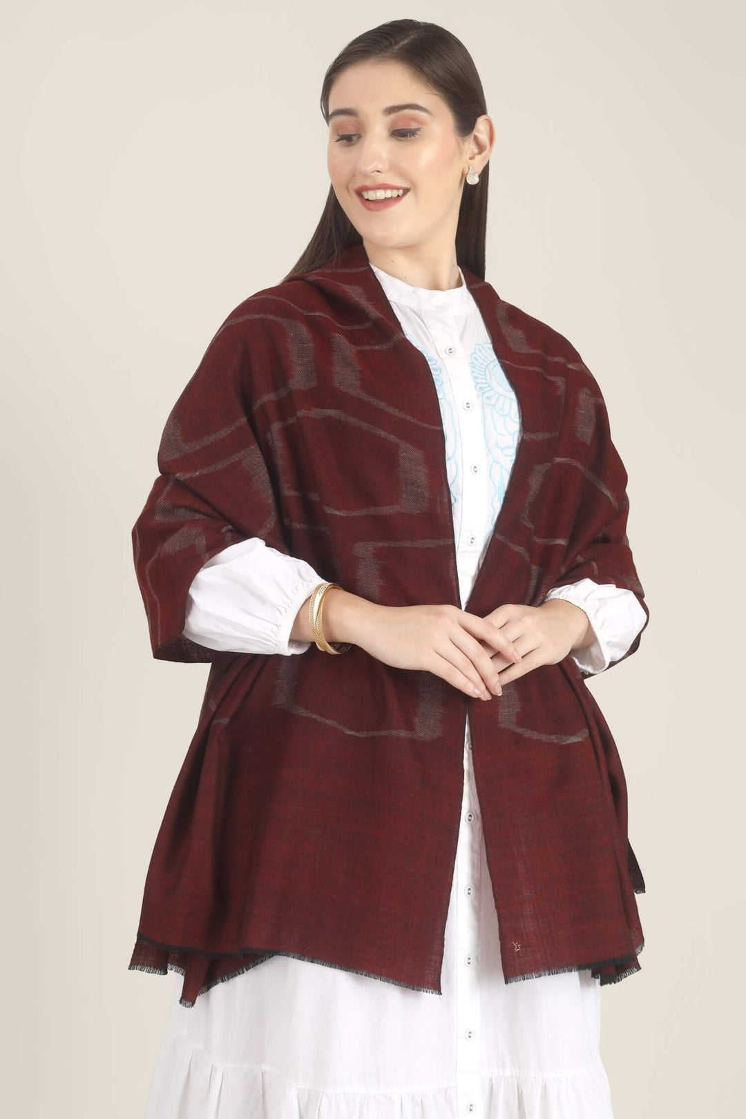 Model draped in a maroon Pure Kashmiri Pashmina shawl with a woven silvery grey geometric pattern over a white dress with light blue embroidery.