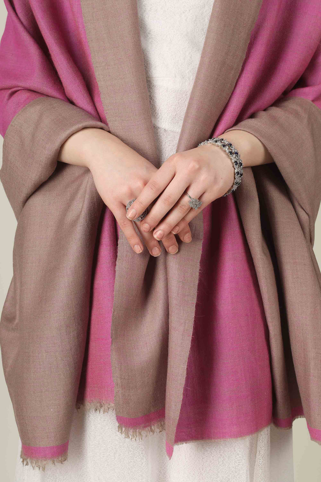 This reversible pashmina shawl pairs a sophisticated dusty taupe with a vibrant fuchsia pink, giving you two distinct looks in one luxurious wrap. 