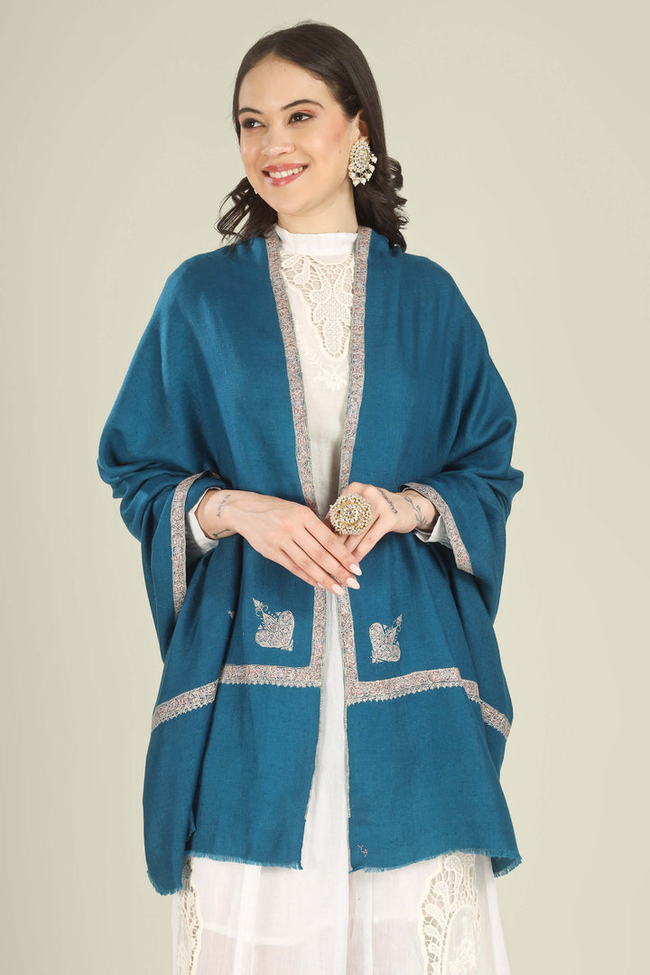 A woman wearing a teal blue shawl with silver embroidered borders over a white embroidered top, photographed against a plain light beige studio background.
    
      | pashmina shawls online | authentic Kashmiri pashmina shawl online | pure pashmina shawl online | original GI certified pashmina shawl online | luxury men's pashmina shawl online from Kashmir | where to buy online pure pashmina in India
    
    | GI Tag Certified - Government-verified authentic Kashmiri Pashmina
    | G20 Official Partner - Selected by India for G20 Summit gifting
    | Handicraft Registered - Official recognition of traditional craftsmanship
    | Certificate of Authenticity - Every purchase includes GI certification