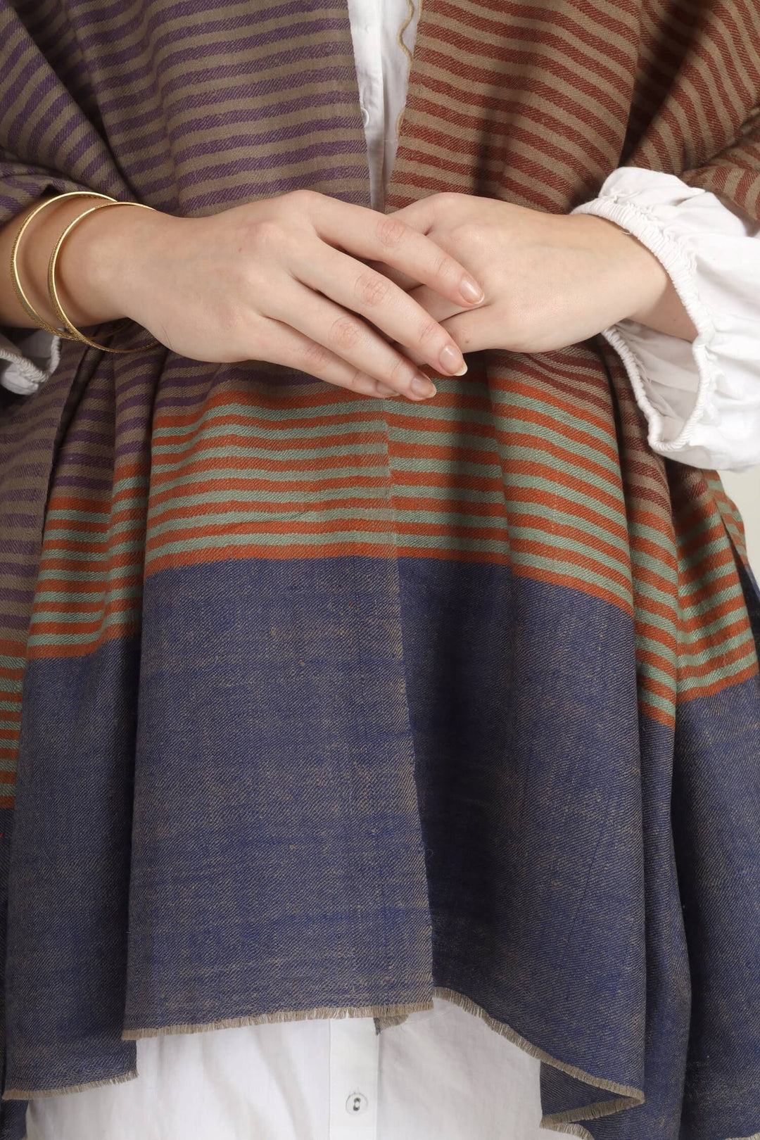 Model draped in a multicolour Pure Kashmiri Pashmina shawl with woven grey-green, plum, brown and rust stripes and a wide plain navy border over a white embroidered dress.