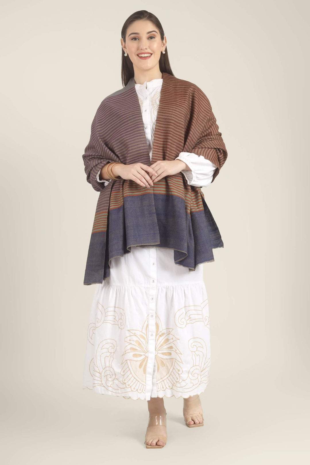 Model draped in a multicolour Pure Kashmiri Pashmina shawl with woven grey-green, plum, brown and rust stripes and a wide plain navy border over a white embroidered dress.