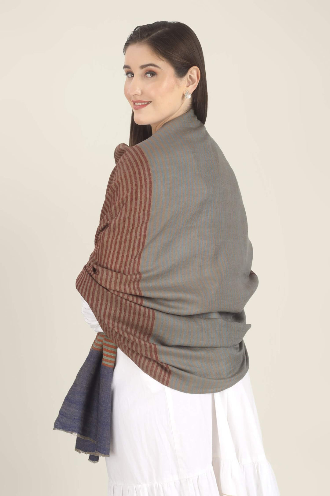 Model draped in a multicolour Pure Kashmiri Pashmina shawl with woven grey-green, plum, brown and rust stripes and a wide plain navy border over a white embroidered dress.