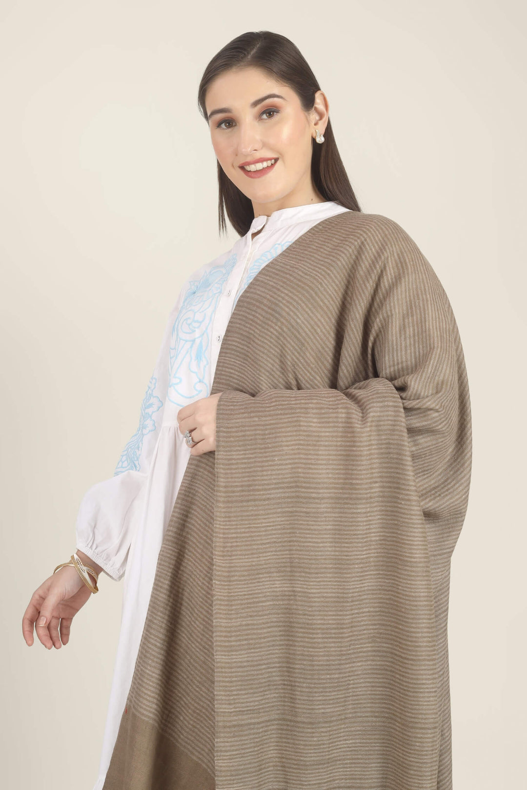 Model draped in a taupe Pure Kashmiri Pashmina shawl with fine woven pinstripes and a wide plain border over a white dress with light blue embroidery.