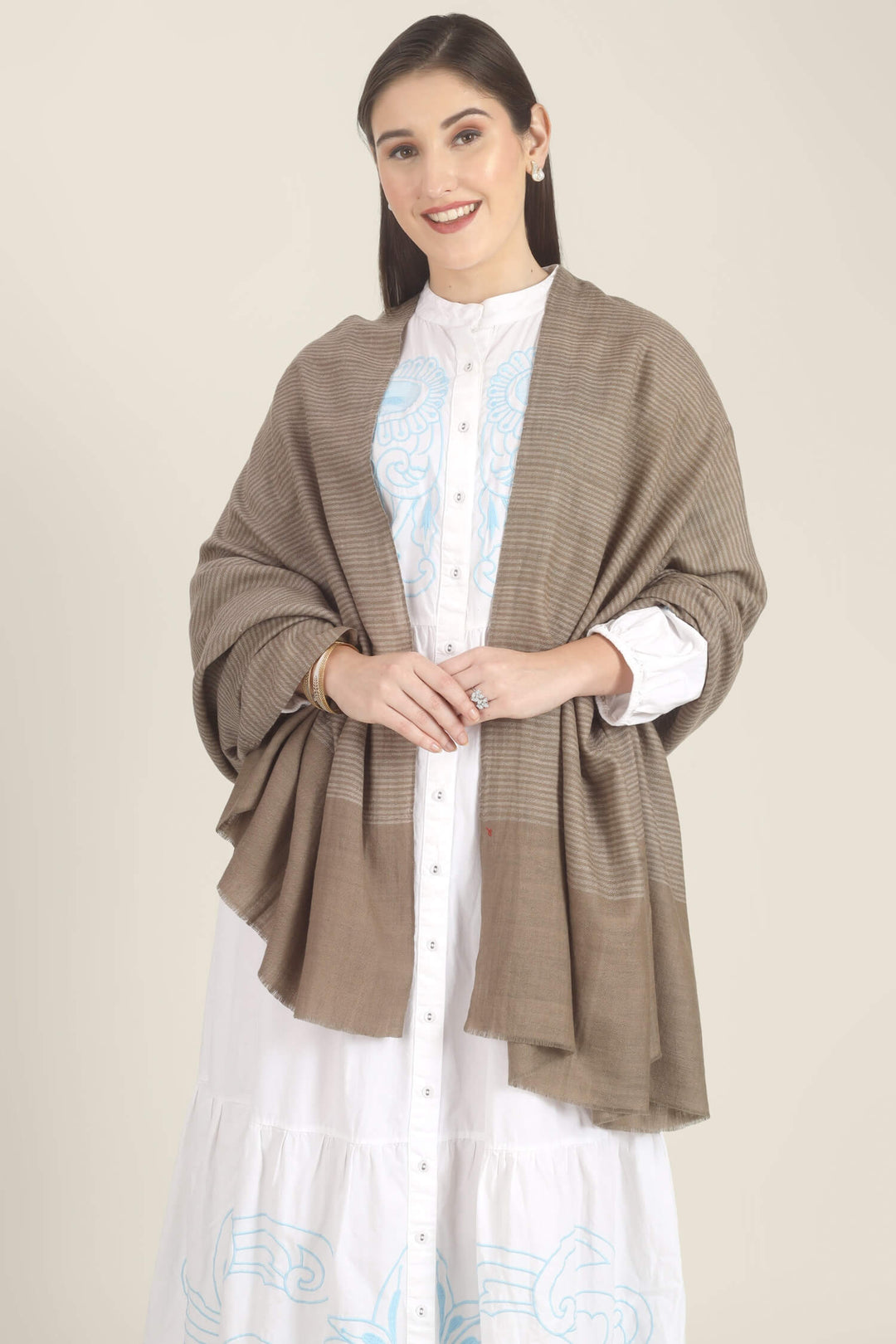 Model draped in a taupe Pure Kashmiri Pashmina shawl with fine woven pinstripes and a wide plain border over a white dress with light blue embroidery.