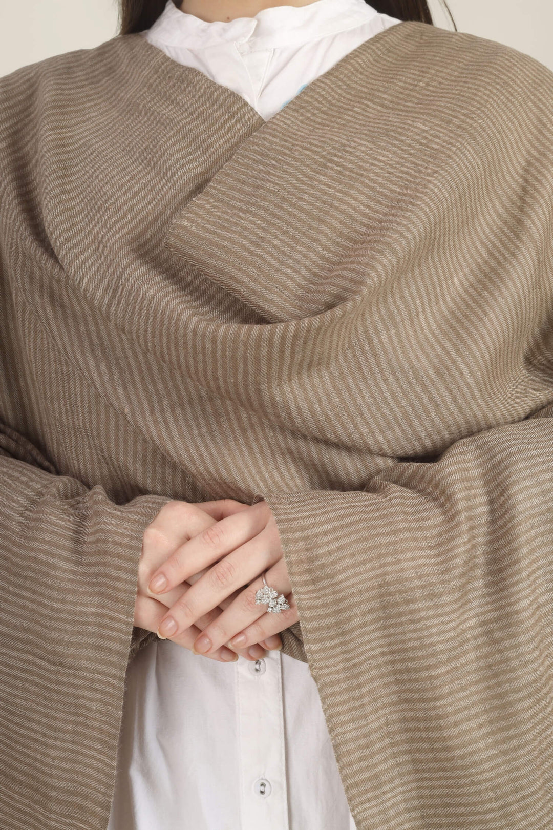 Model draped in a taupe Pure Kashmiri Pashmina shawl with fine woven pinstripes and a wide plain border over a white dress with light blue embroidery.