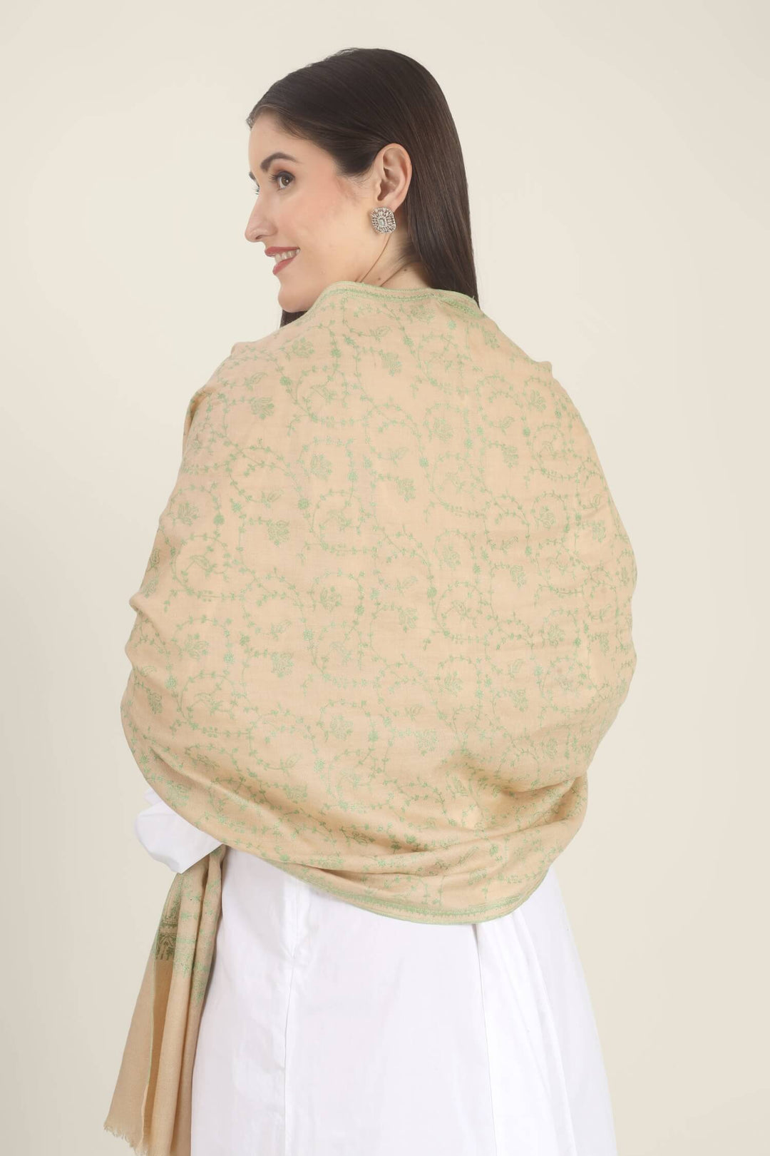 Model wearing a beige GI Kashmiri Pure Pashmina stole with soft green floral jaal Sozni embroidery over a white outfit.