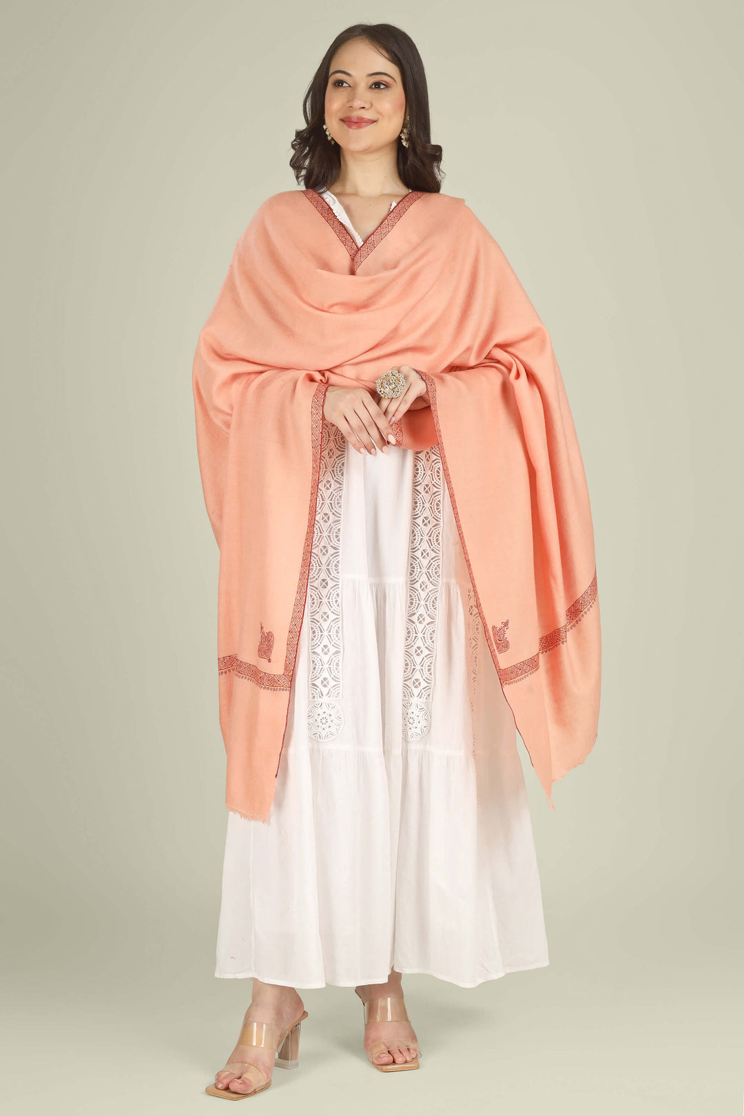 This Peach GI Kashmiri Pure Pashmina Raiha Hashidaar Shawl comes in a soft peach base highlighted with a geometric hashidaar border and a single ornate corner motif, giving a clean, modern look with a touch of traditional detail.
