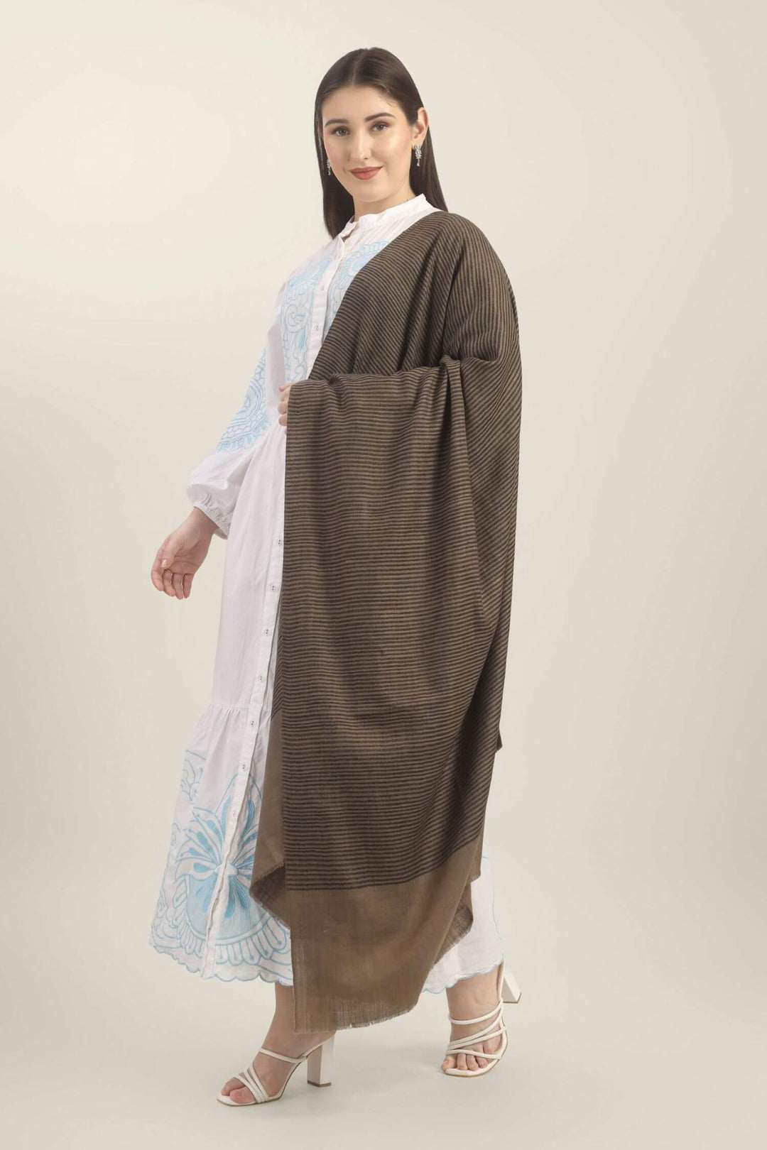 Model holding a taupe Pure Kashmiri Pashmina shawl with fine black woven stripes and a wide plain border over a white embroidered dress.
