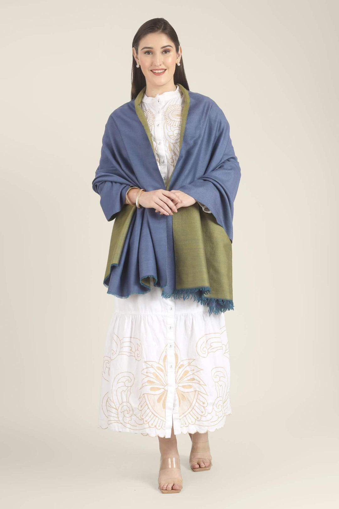 Model wearing a blue and olive-green reversible Pure Kashmiri Pashmina shawl with teal fringe over a white embroidered dress.
