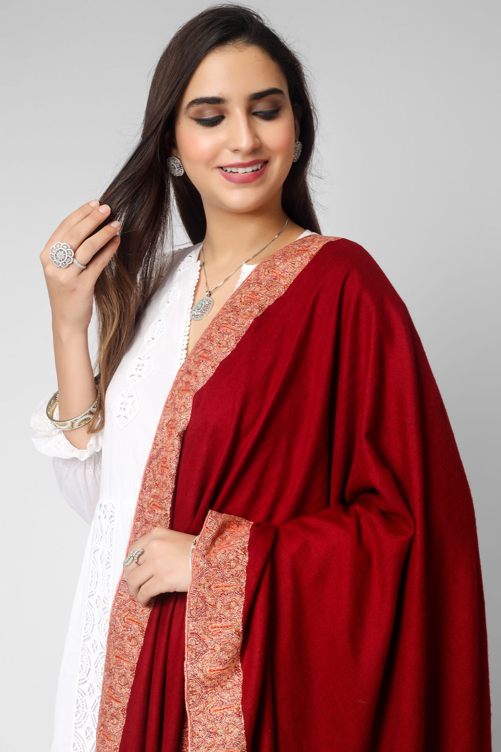 This bright maroon handmade Kashmiri pashmina shawl is made of the finest pashmina wool and has gorgeous Sozni embroidery done on all four sides in the conventional Dordaar pattern to wrap you in luxury. The shawl is enhanced by the delicate and exquisite needlework, which elevates its tradition.