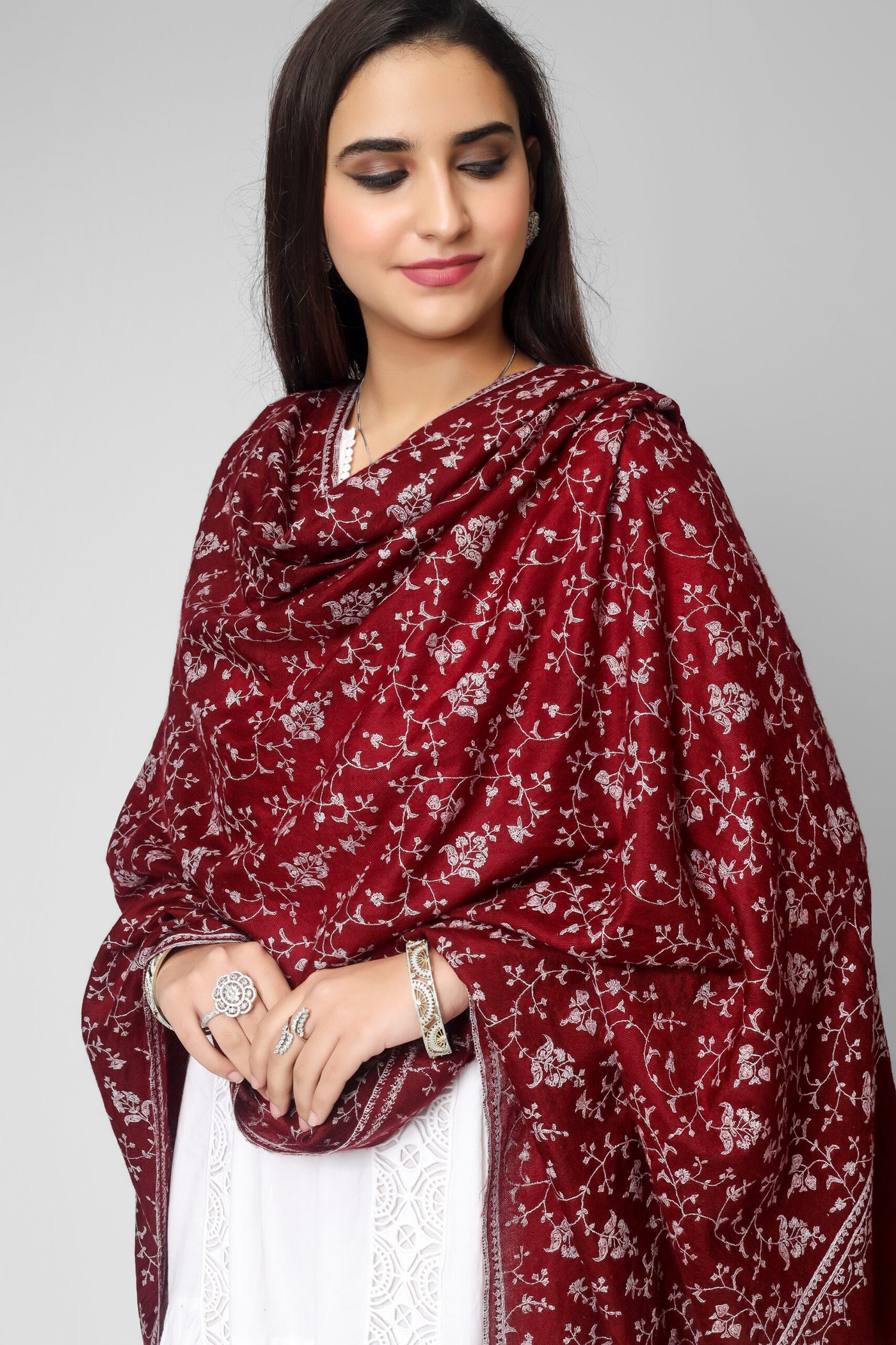 The embroidery is typically done by hand, using a needle and thread in shades of fade gray, which creates a beautiful and subtle contrast against the deep maroon color. The result is a stunning and sophisticated shawl that can be worn on special occasions or as a statement piece with any outfit.